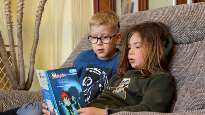 Zwei Schüler sitzen gemütlich auf einem Sessel und lesen gemeinsam in dem Buch "Hilfe, ich bin ein Vampir".