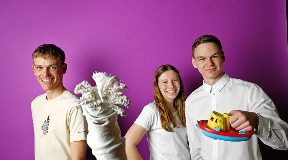 Arian Niclas Wulf, Luise Koball und Luca Steven Sauck aus Mecklenburg-Vorpommern posieren vor einer lila Wand mit einem Spielzeugboot und einem Kalkröhrenwurm aus Stoff.