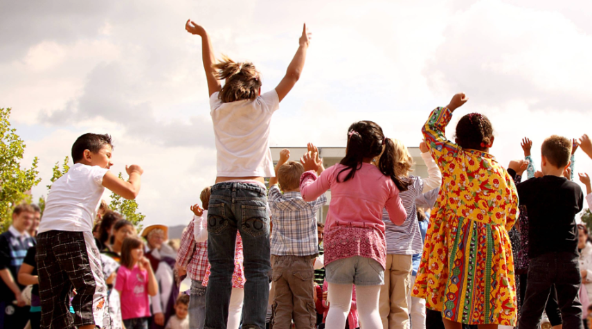 Gruppe von Kindern springt und jubelt bei einer Outdoor-Veranstaltung, während im Hintergrund weitere Menschen zuschauen.