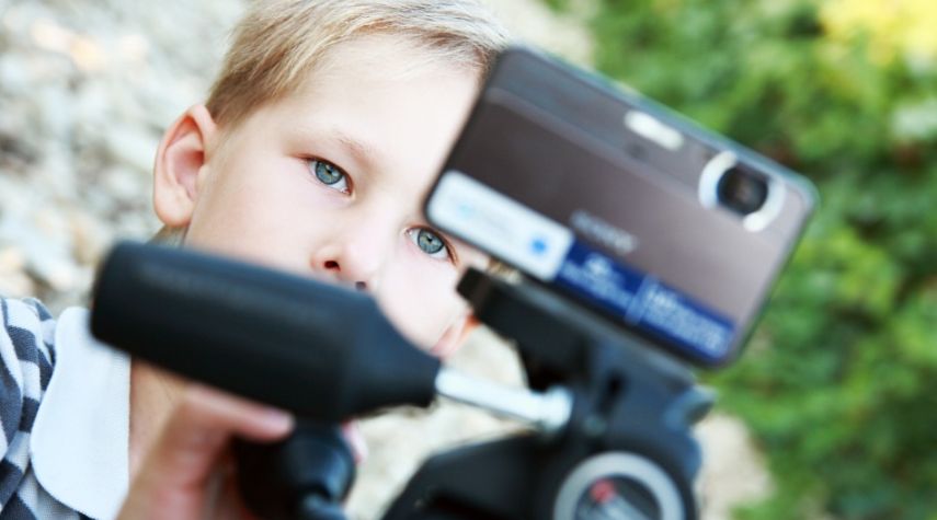 Nahaufnahme eines Kindes, das konzentriert durch eine Kamera auf einem Stativ blickt.