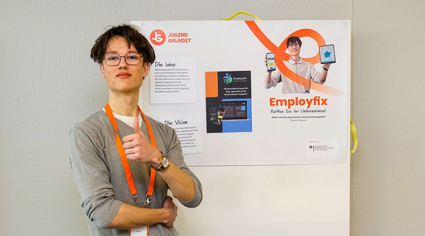 Eine Person mit Brille und orangefarbenem Band zeigt Daumen hoch vor einem Präsentationsposter mit dem Titel „Employfix“.