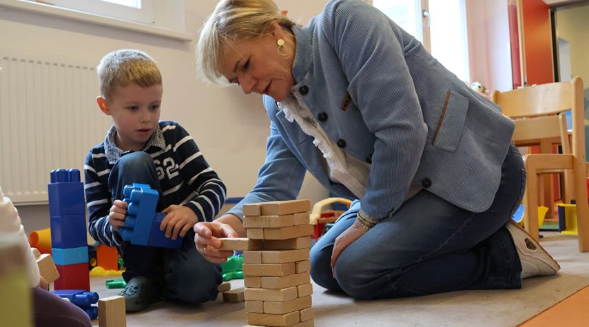 Bildungsministerin Simone Oldenburg und ein Kind der Kita Seestern knien auf dem Boden. Sie bauen gemeinsam mit Holz- und Kunststoffbausteinen einen Turm.