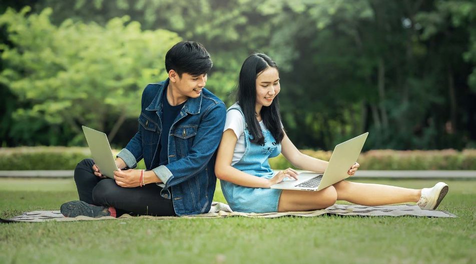 Asiatisches Paar sitzt im Park und nutzt einen Laptop, um gemeinsam zu arbeiten oder Informationen zu suchen.