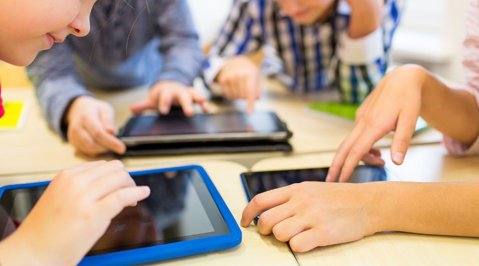 Mehrere Kinder sitzen an einem Tisch und bedienen Tablets mit ihren Fingern. Die Szene zeigt eine Lernumgebung mit moderner Technologie.