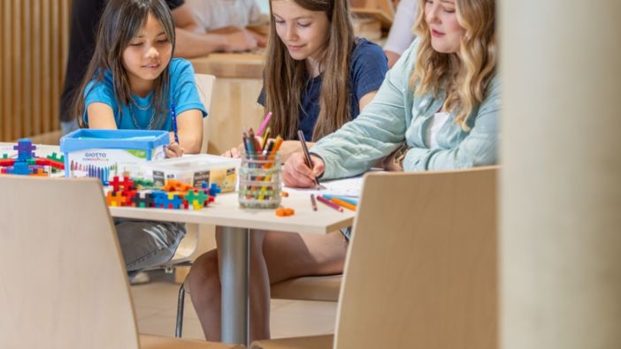 Kinder sitzen in einer Kita an einem Tisch und malen zusammen in einem kreativ gestalteten Raum. Kinder sitzen in einer Kita an einem Tisch und malen zusammen in einem kreativ gestalteten Raum.