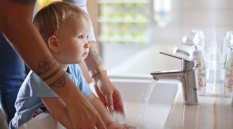 Eine Erzieherin hilft einem kleinen Kind am Kinderwaschbecken beim Waschen der Hände.