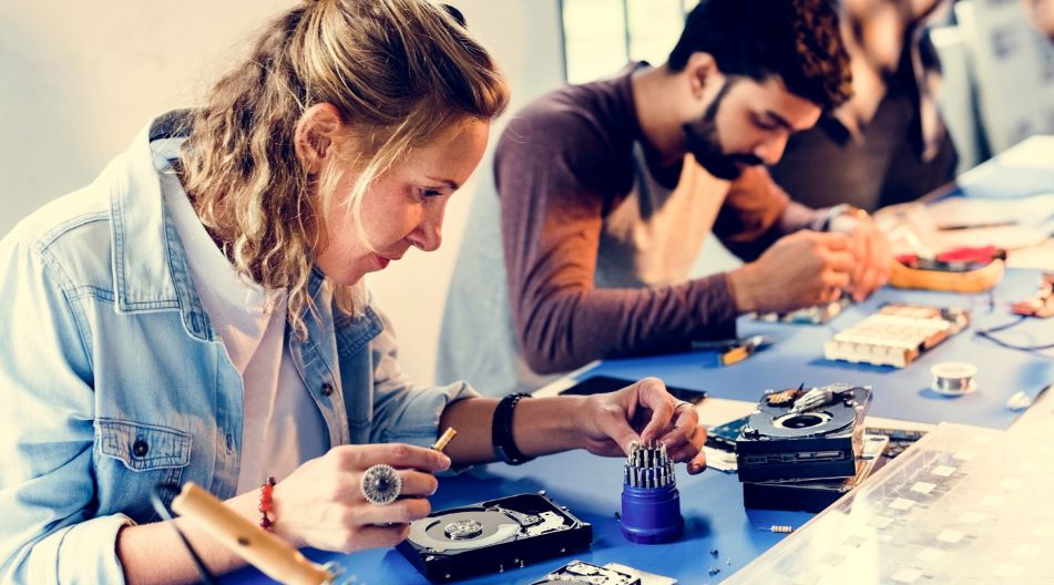 Junge Menschen arbeiten an Festplatten für Computer mit feinen Werkzeugen.