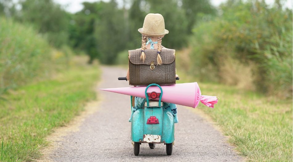 Ein Mädchen fährt auf einem Roller mit ihrer Schultüte einen Weg entlang.