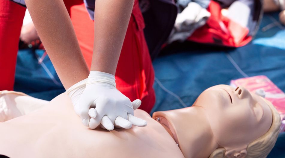 Eine Person übt an einer Reanimationspuppe eine Herzdruckmassage, trägt dabei Handschuhe.