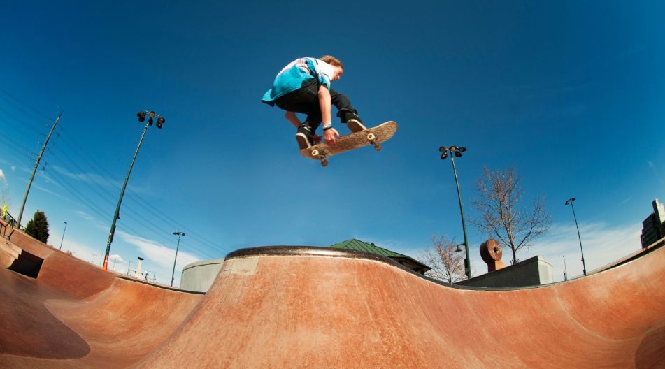 Skateboarder springt hoch über eine Rampe in einem Skatepark vor blauem Himmel.
