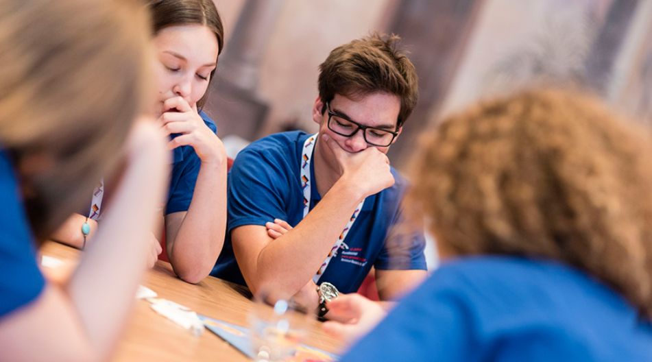 Schülerinnen und Schüler sitzen an einem Spieltisch und denken nach.