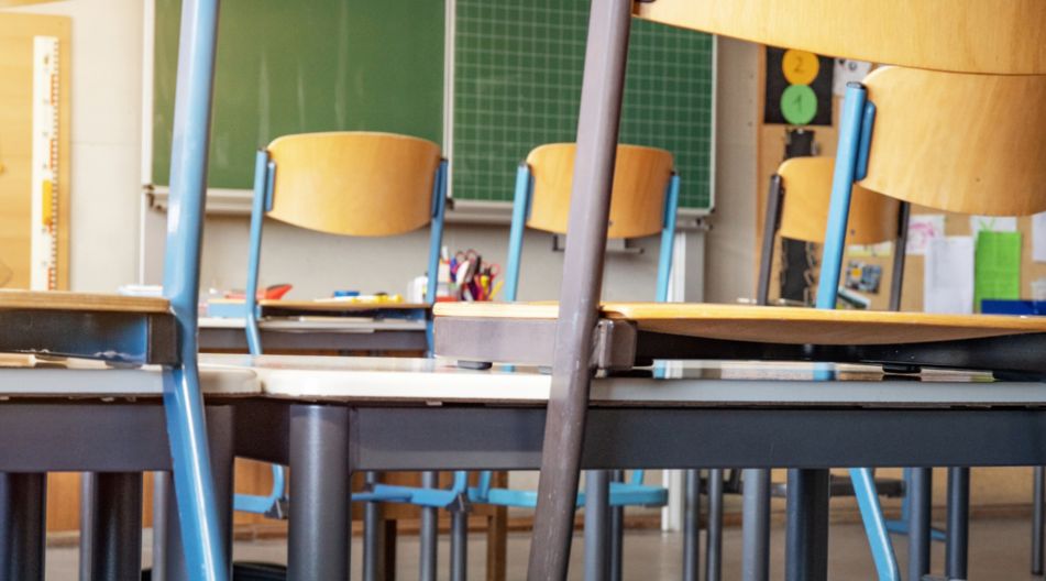 Ein leeres Klassenzimmer mit hochgestellten Stühlen auf den Tischen vor einer grünen Tafel.