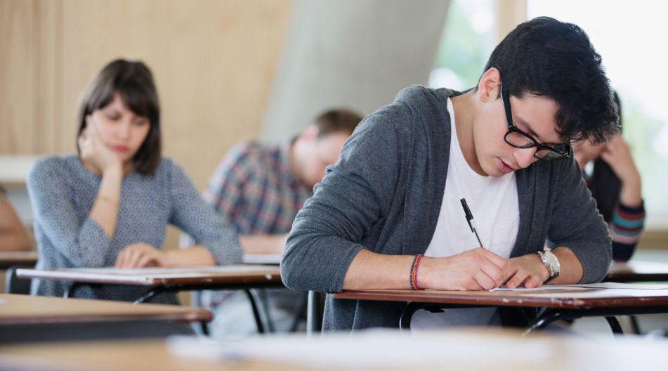 Mehrere Studierende sitzen in einem Prüfungsraum an Tischen und schreiben konzentriert eine Klausur.