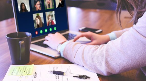 Eine Frau sitzt mit einem Laptop am Schreibtisch und hält eine Videokonferenz ab