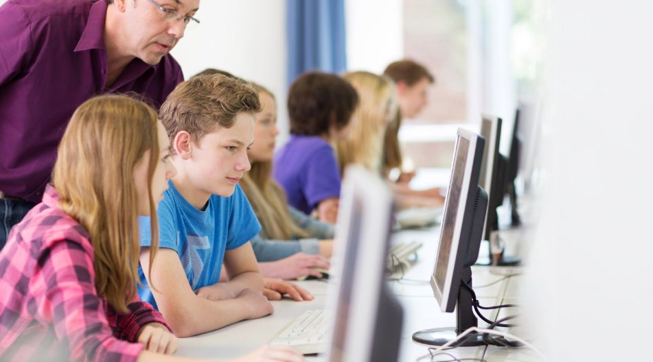 Ein Mann und mehrere Kinder sitzen vor Computern und arbeiten gemeinsam an einem Projekt.