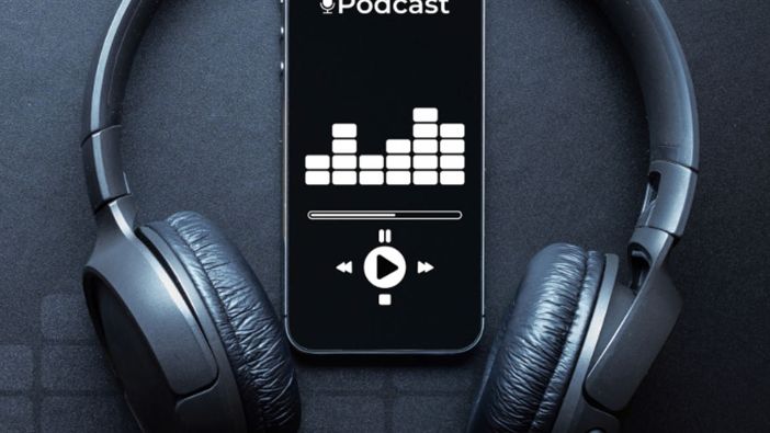 Ein Smartphone liegt mit geöffneter Podcast-App auf einem schwarzem Hintergrund. Um das Smartphone herum sind Kopfhörer.