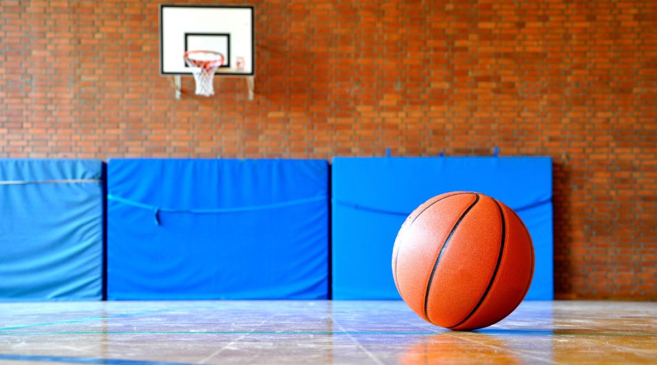 Ein Basketball liegt allein in einer Sporthalle. An der Wand sind Weichbodenmatten zu sehen.