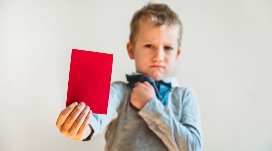 Ein Kind hält eine Rote Karte in die Kamera und steht im Hintergrund.